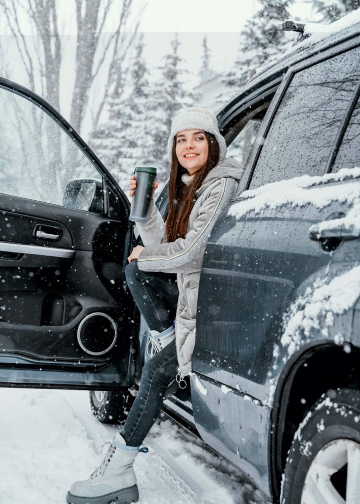foto de uma mulher a beber um café dentro de um carro no meio da neve